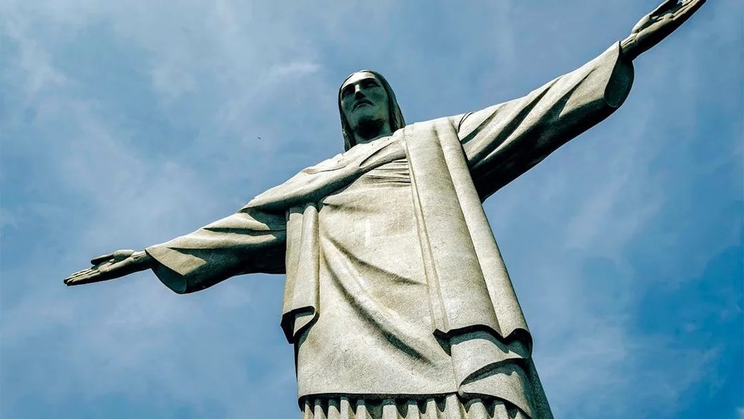 Christ the Redeemer statue with outstretched arms against blue sky, Rio de Janeiro, Brazil.