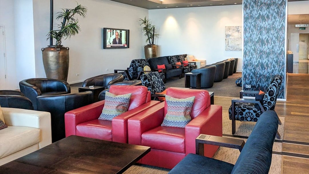 Plaza Premium Lounge seating area with red and black chairs, TV, and decorative plants.