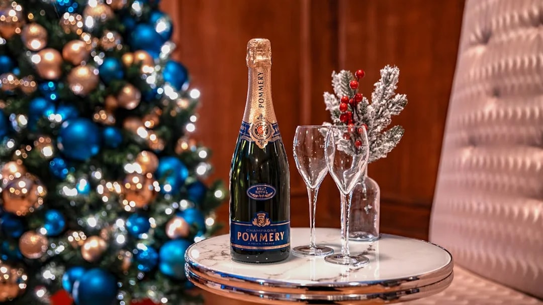 Champagne bottle and glasses on table with Christmas tree in background, London tour experience.