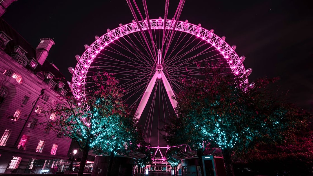 London Eye illuminated at night with nearby building and trees.