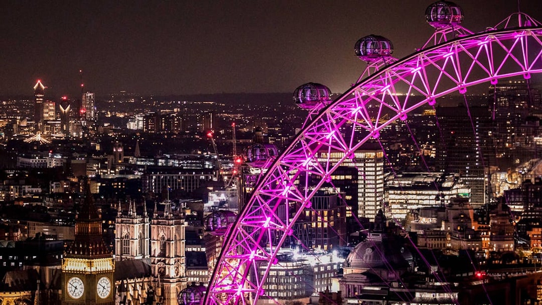 London Eye illuminated at night with city skyline in the background.
