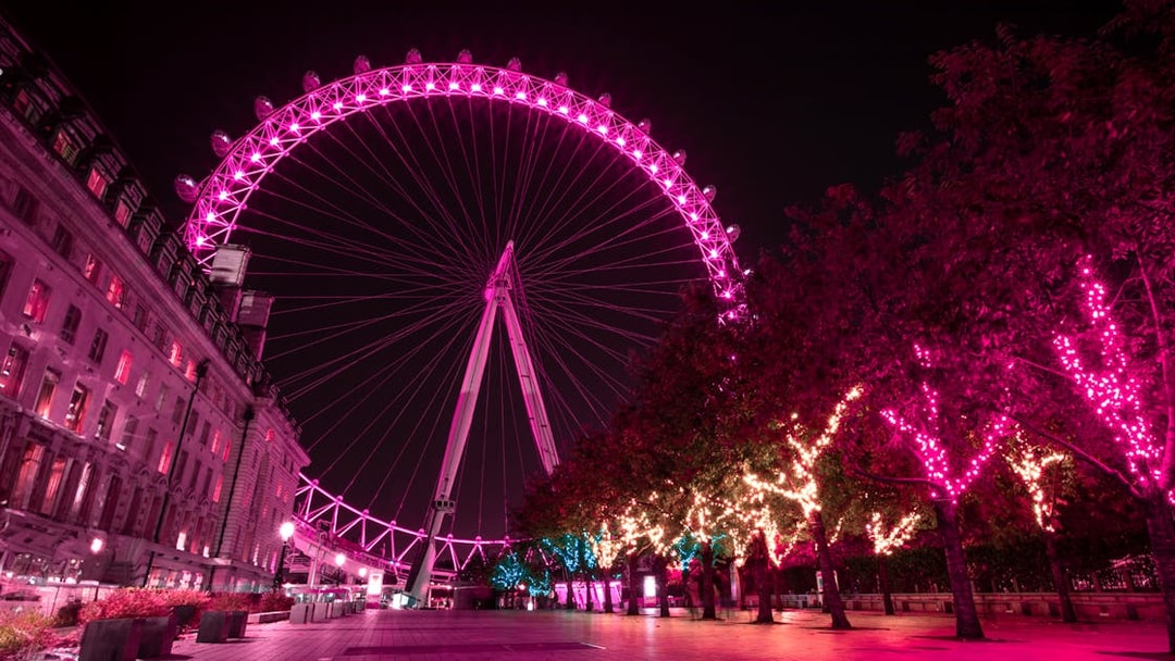 London Eye illuminated at night with vibrant pink lights, view from the riverside walkway.