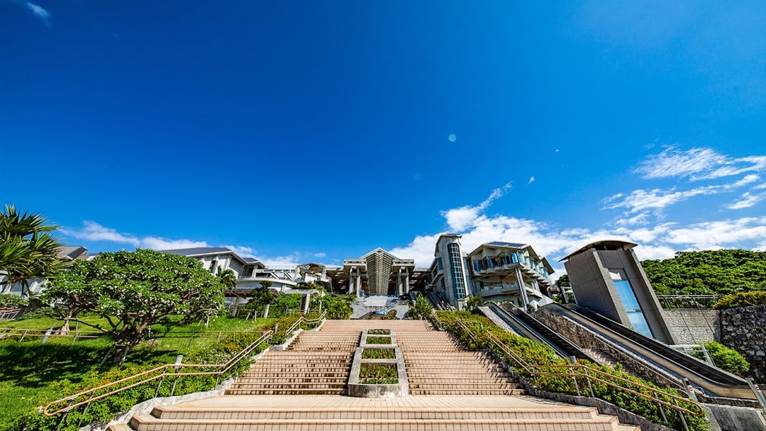 Churaumi Aquarium entrance with stairs and escalators under a clear blue sky.