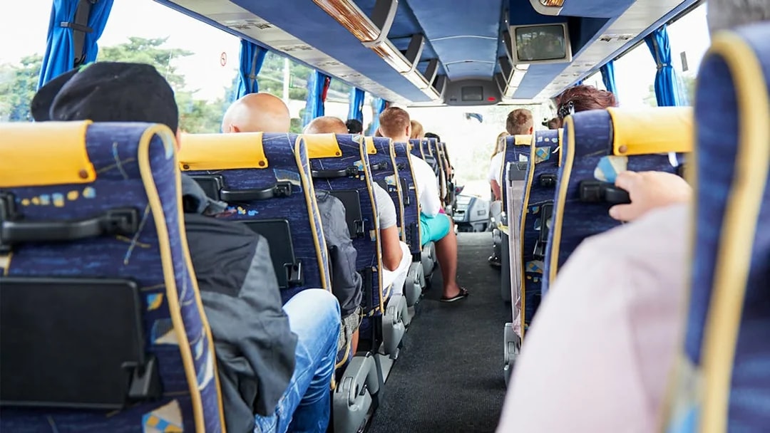 Passengers seated on a tour bus with blue and yellow seats.