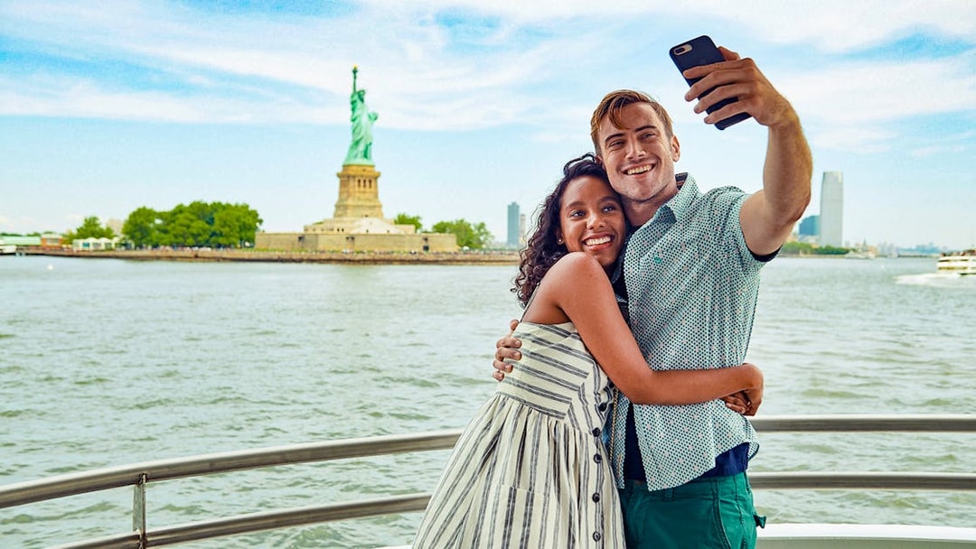 Guests taking a selfie on a boat with the Statue of Liberty in the background.