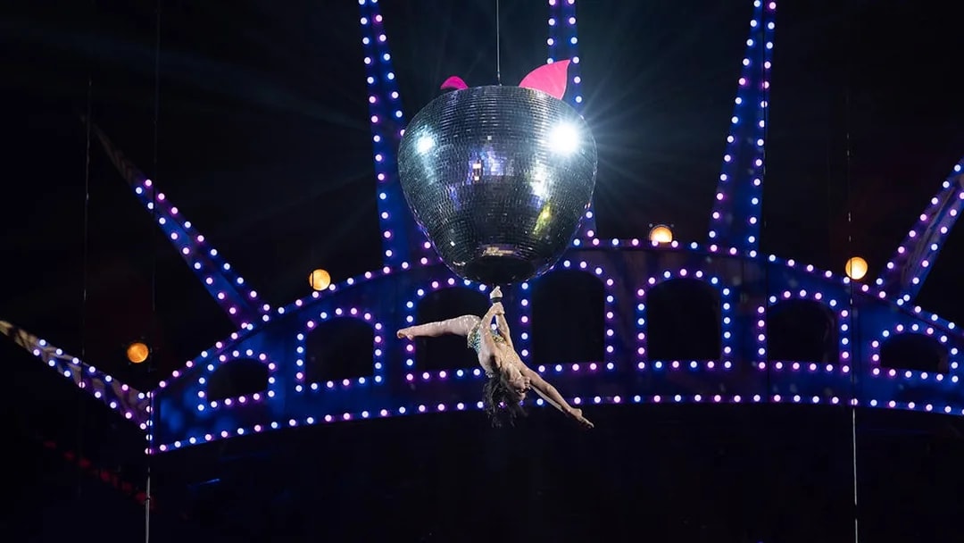 Performer hanging from a disco ball in Mad Apple show.