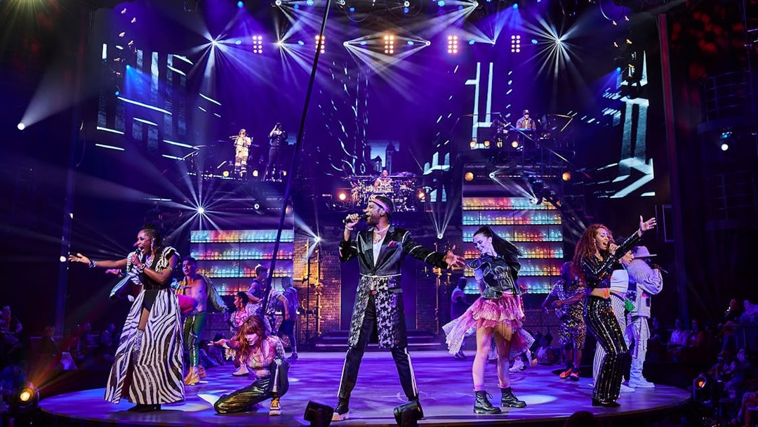 Performers on stage during the Mad Apple show with vibrant lights and costumes.
