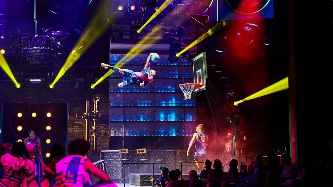 Performer dunking basketball during Mad Apple show in New York City theater.