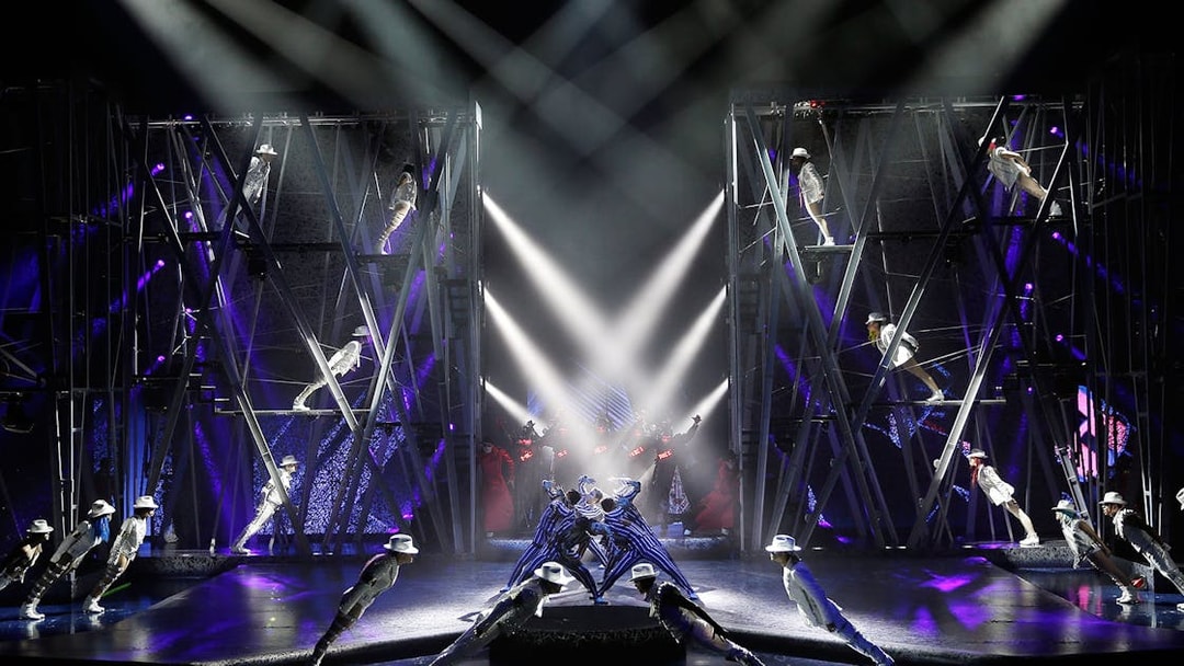 Performers in white suits and hats lean forward on stage during Michael Jackson ONE show.