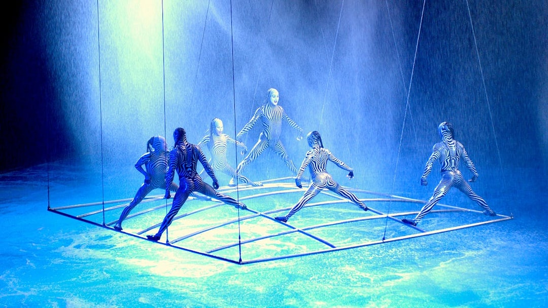 Performers in striped costumes on a suspended grid in a water-themed show.