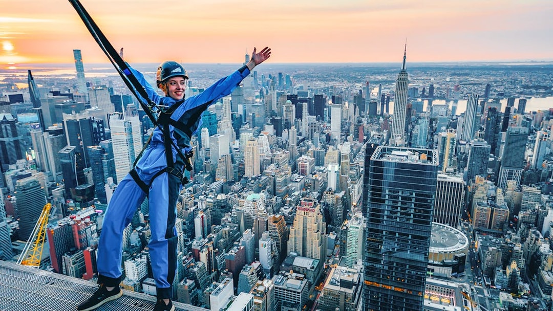 Person harnessed on skyscraper edge with New York City skyline in background during City Climb Experience.