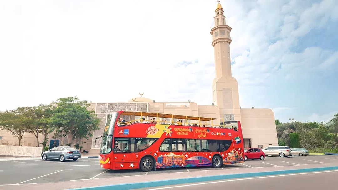 Red double-decker bus on Abu Dhabi hop-on hop-off tour near a mosque.
