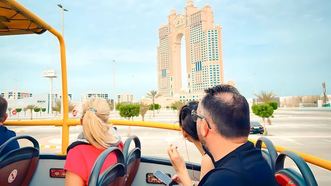 Hop on hop off bus tour near Rixos Marina Abu Dhabi with passengers viewing skyline.