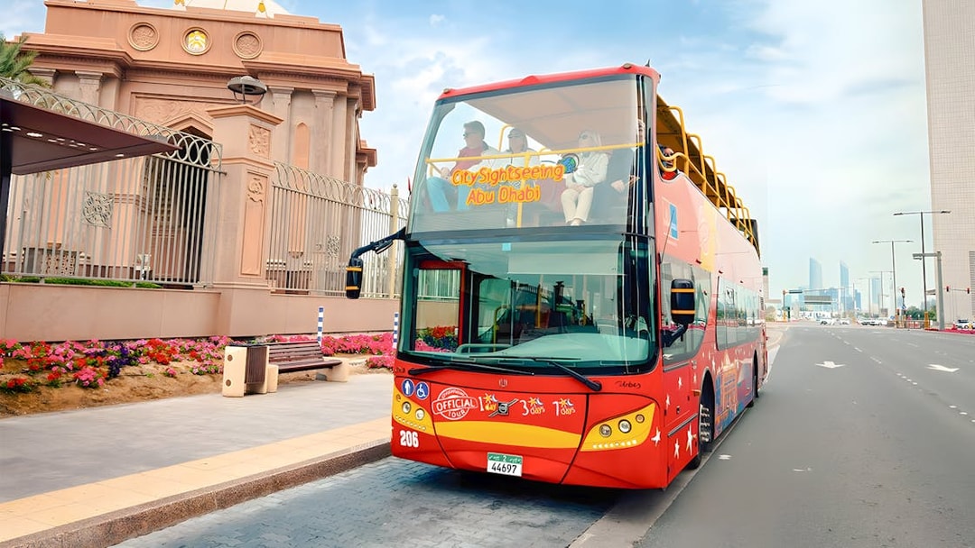 City Sightseeing hop-on hop-off bus in Abu Dhabi near a historic building.