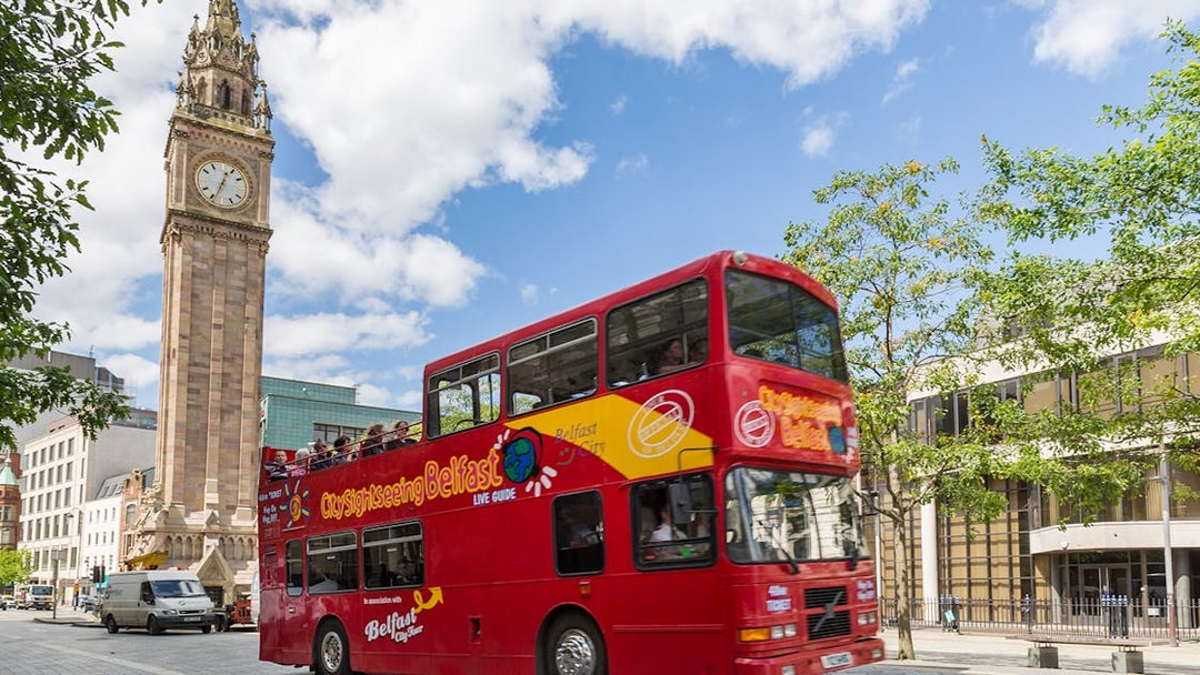 Red double-decker bus on Belfast Hop-On Hop-Off Tour passing Albert Memorial Clock.