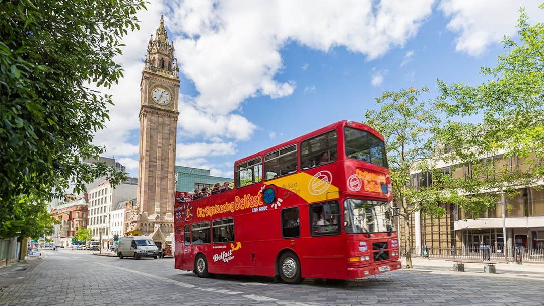 Red double-decker bus near Belfast's Albert Memorial Clock on sightseeing tour.
