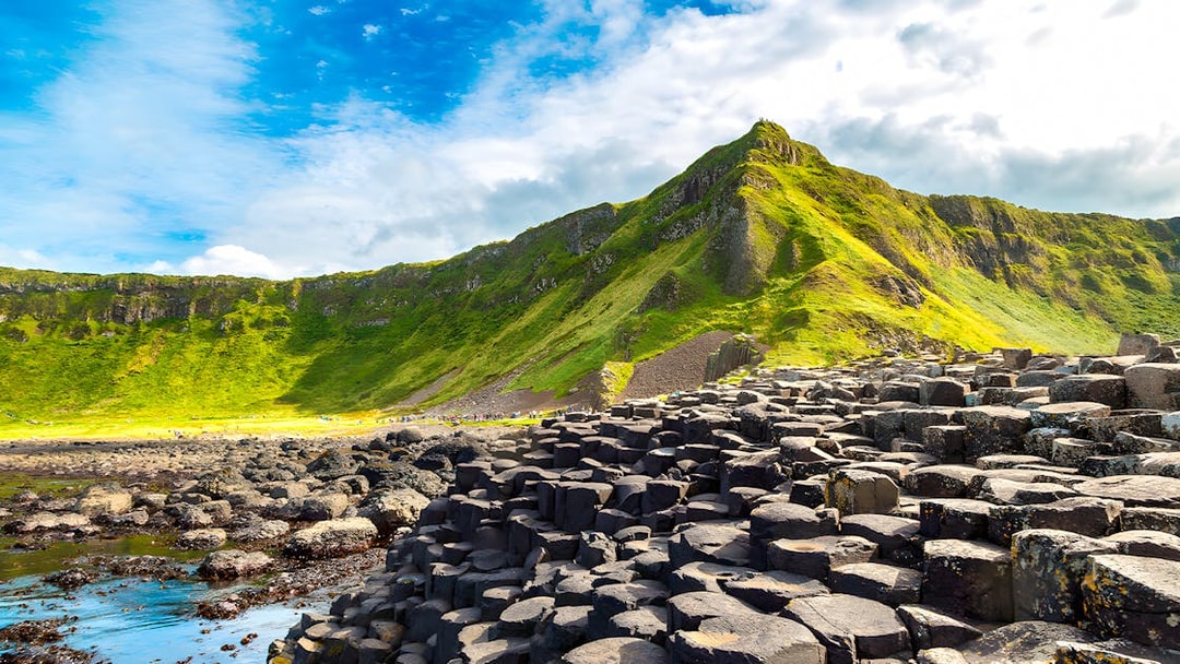 Giant’s Causeway basalt columns with green cliffs in the background, Northern Ireland.
