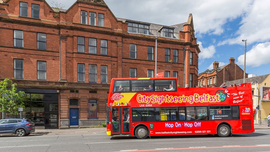 Belfast city tour bus passing by a historic brick building near The Bakery.