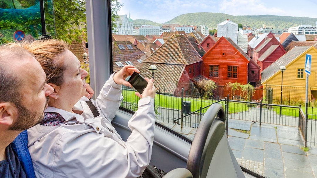 Tourists on Bergen Hop on Hop off bus viewing colorful wooden houses in Bergen, Norway.