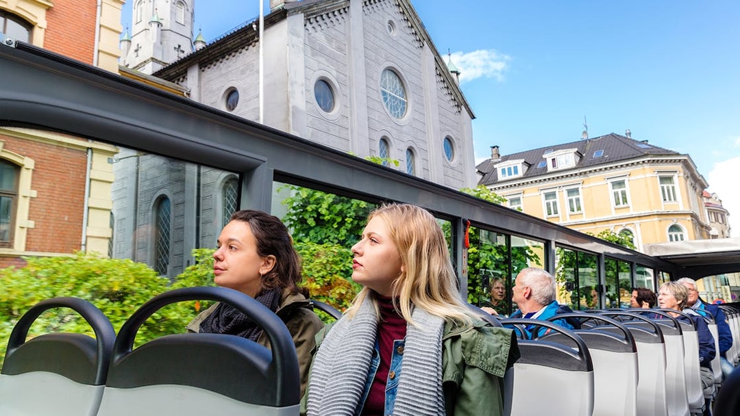Tourists on Bergen Hop on Hop off bus passing historic buildings.
