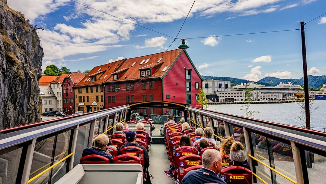 Bergen Hop on Hop off bus with tourists passing colorful waterfront buildings.