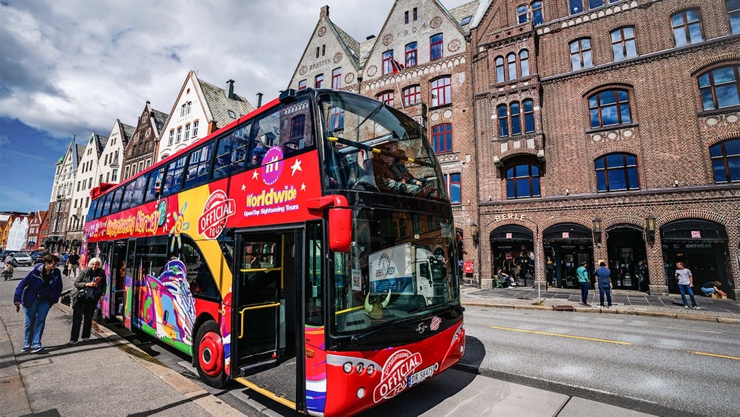Bergen hop-on hop-off bus in front of historic Bryggen buildings.