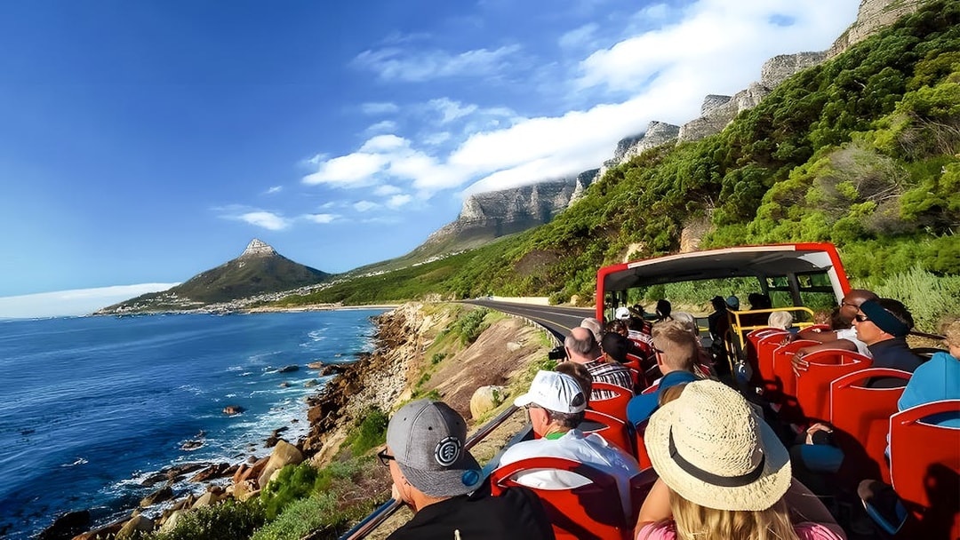 Open-top bus tour along ocean road with view of Lion's Head and Table Mountain, Cape Town.