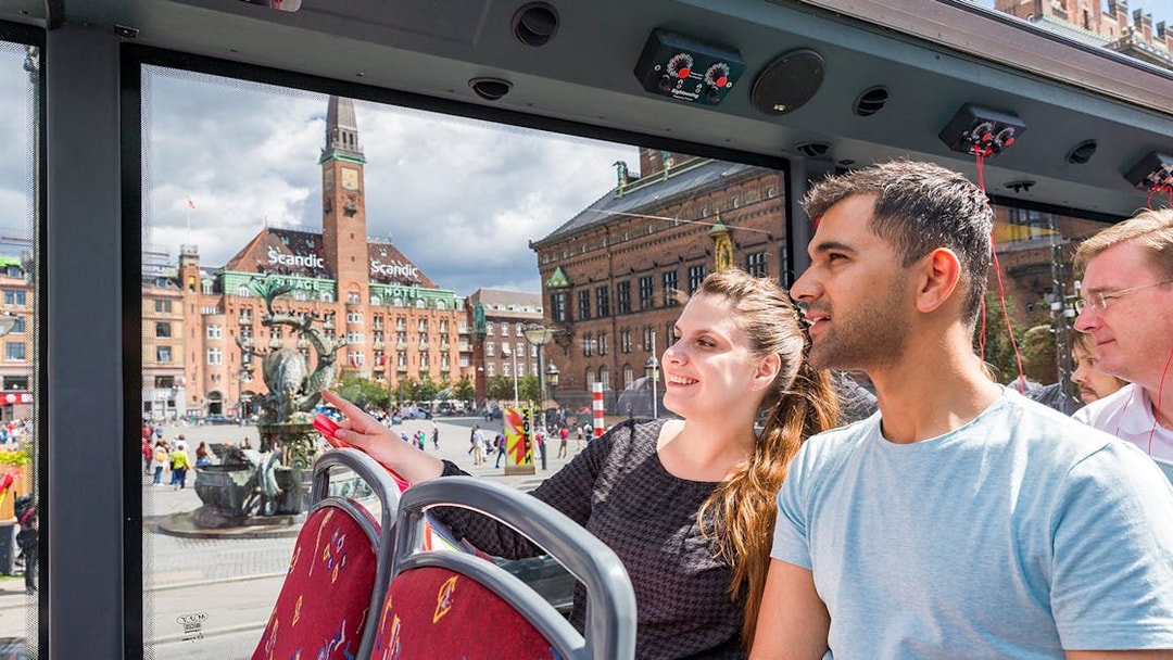 Couple enjoying Copenhagen Hop-On-Hop-Off bus tour with city square view.