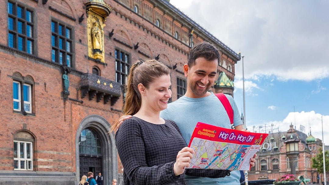 Friends examining Copenhagen HOHO bus route map near historic building.