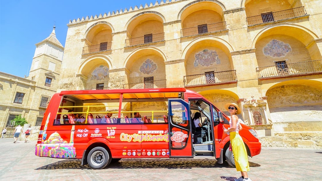 Woman waiting outside hop-on hop-off mini bus in front of historic building in Córdoba, Spain.