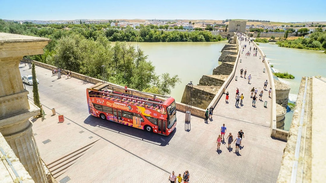 Open-top sightseeing bus near Roman Bridge in Cordoba, Spain.