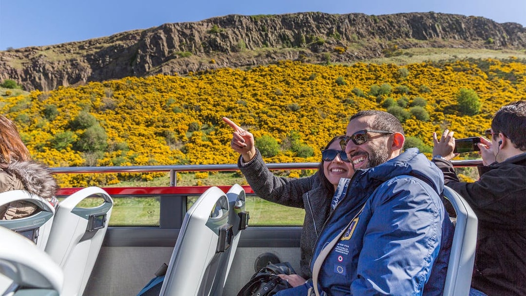 Tourists enjoying a hop-on hop-off bus tour in Edinburgh with views of Arthur's Seat.