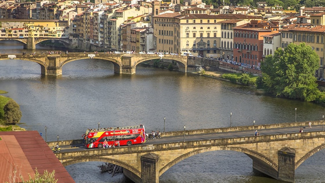 Florence hop-on hop-off tour bus crossing Ponte Vecchio bridge over the Arno River.