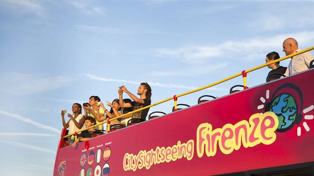 Tourists on open deck of sightseeing bus in Florence, capturing views.