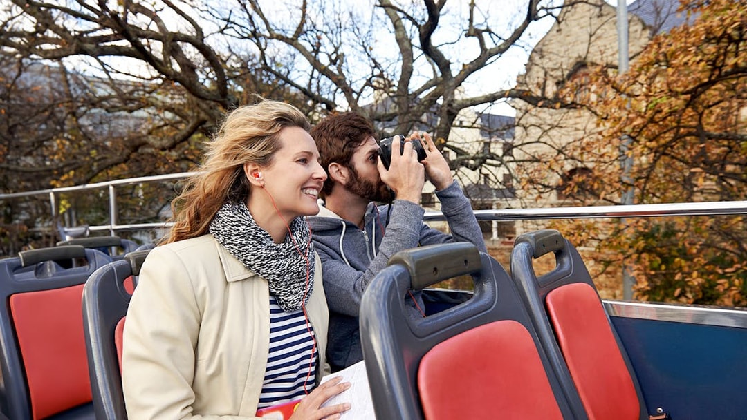 Couple enjoying audio guide on open-top tour bus.