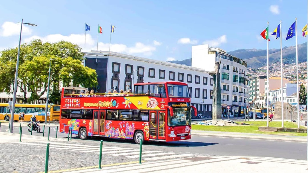 Hop-on hop-off bus in Funchal, Madeira, passing city buildings and flags.
