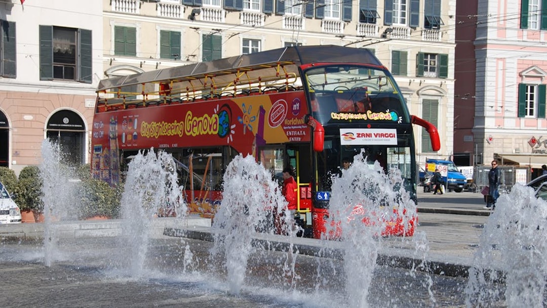 Hop-on-hop-off bus near fountains in Genoa city center.
