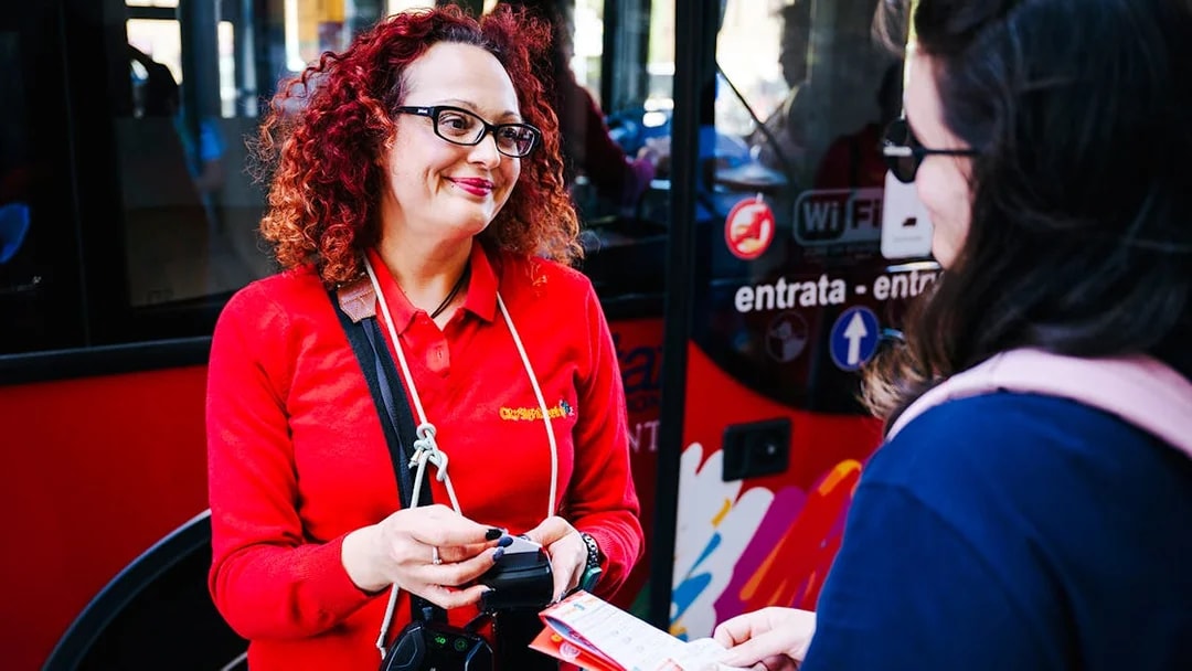Guide assisting tourist with tickets on City Sightseeing Italy bus.