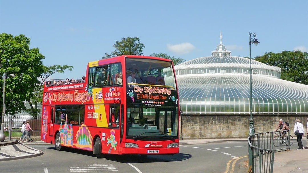Red double-decker bus on Glasgow hop-on hop-off tour near the People's Palace.