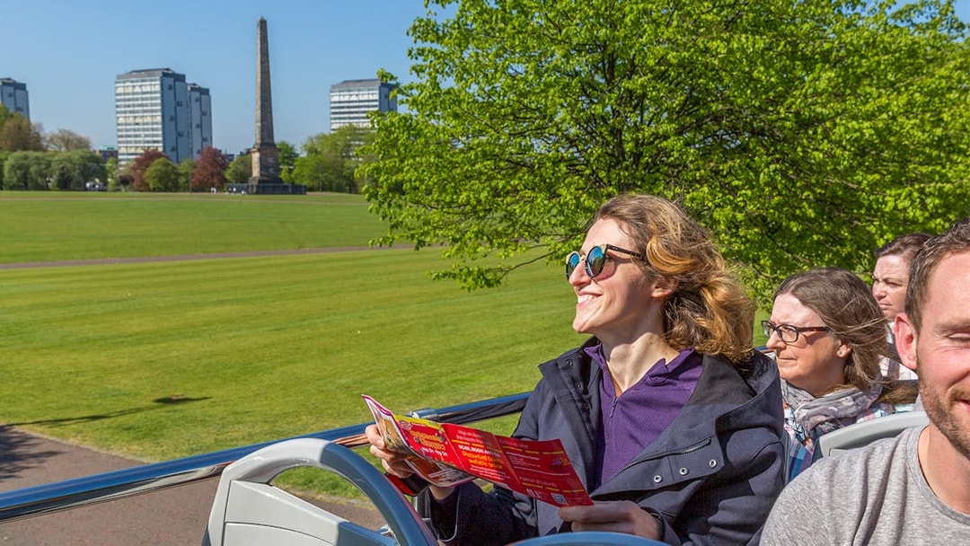 Tourists on an open-top bus in Glasgow, viewing the city's landmarks and greenery.