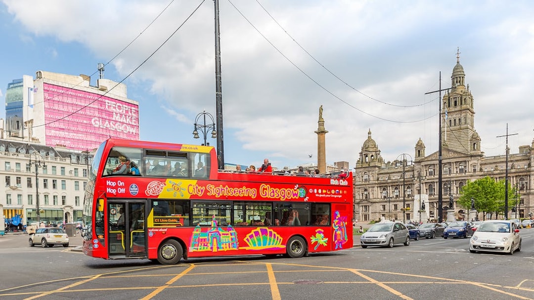 Open-top sightseeing bus in George Square, Glasgow, with City Chambers in the background.