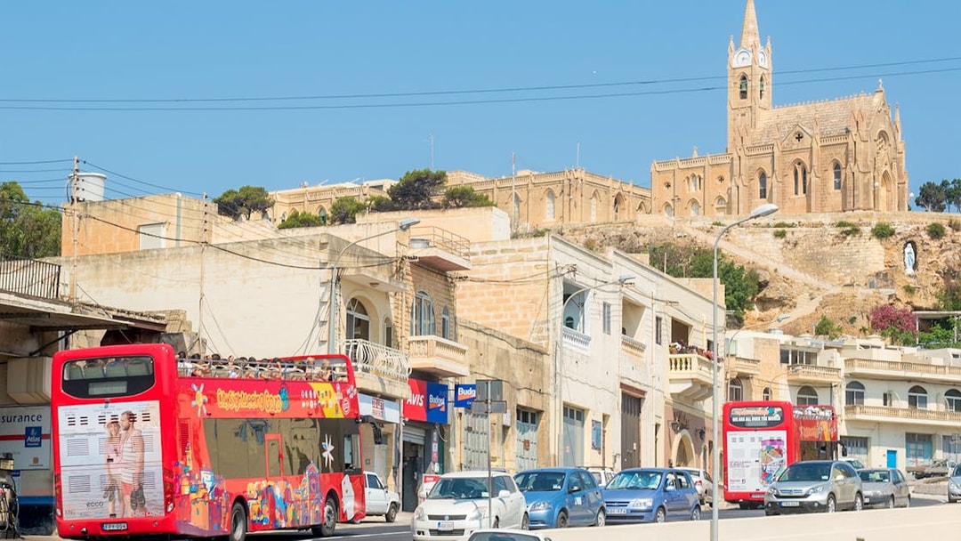Red double-decker bus on Gozo Hop On Hop Off tour passing Ta' Pinu Basilica, Malta.