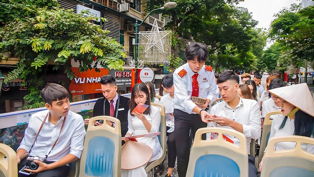 Passengers on Hanoi city hop-on hop-off tour bus reviewing brochures.