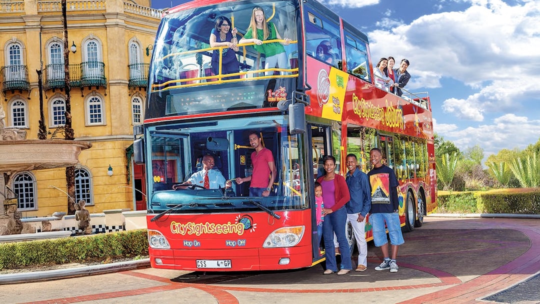 Hop-on hop-off bus with people boarding near a historic building in Johannesburg.