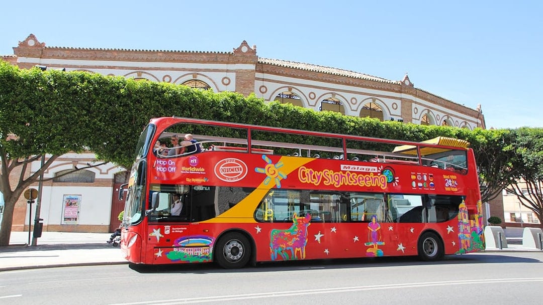 City Sightseeing HOHO bus in Malaga near historic building.