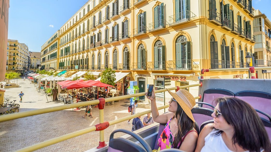 Passengers on Malaga hop-on hop-off tour bus passing historic buildings.