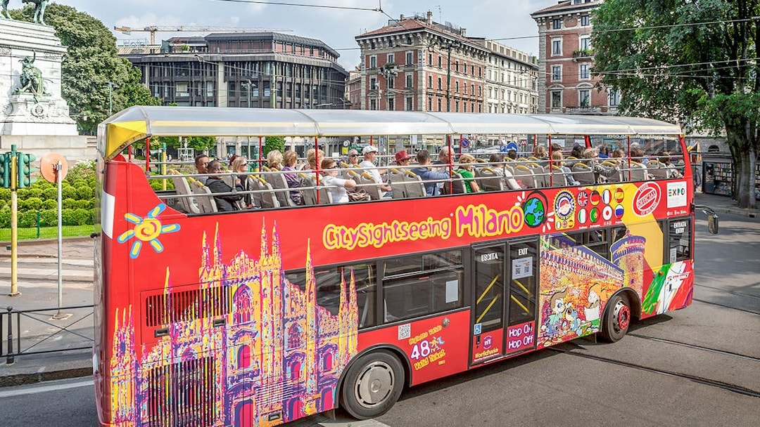 City Sightseeing Milan hop-on hop-off bus with tourists near historical buildings.