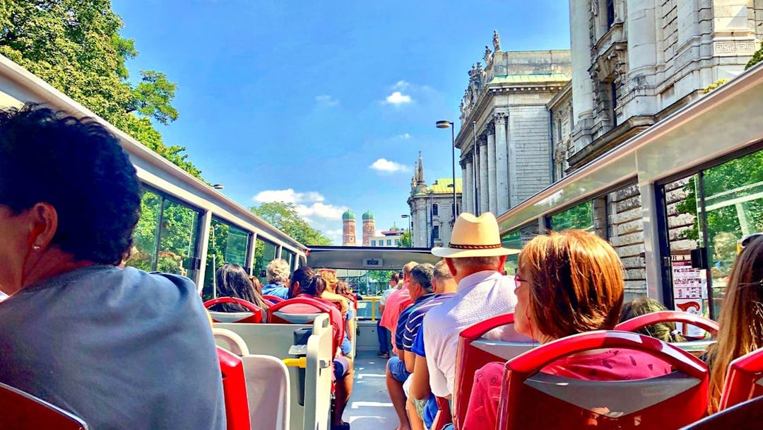 Tourists on an open-top Citysightseeing Munich bus with Frauenkirche in view.