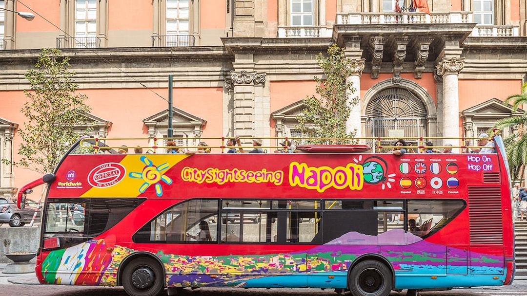 Open-top sightseeing bus in Naples in front of historic building.
