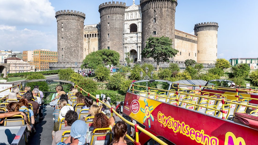 City sightseeing bus near Castel Nuovo, Naples, with tourists on board.